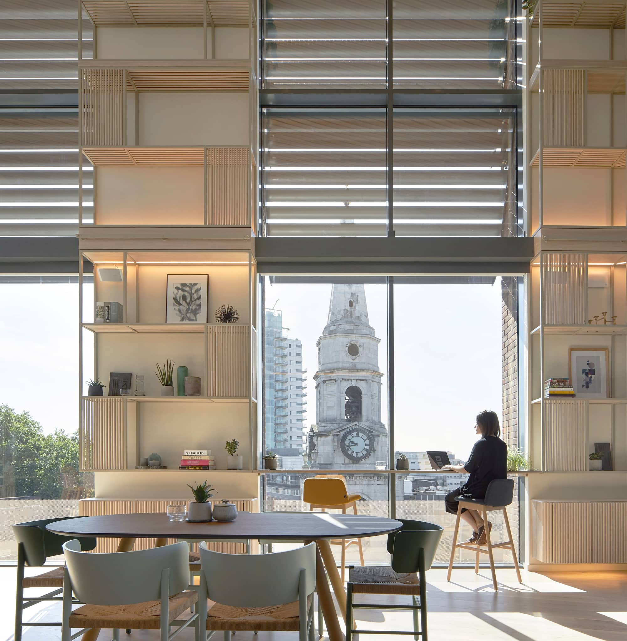 Woman sitting on high chair at the window working in a modern office with high ceilings.